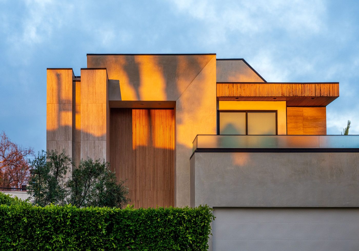 Une maison contemporaine dans la lumière de fin d’après-midi, sa façade de lattes de bois et de béton réchauffée par le soleil bas.