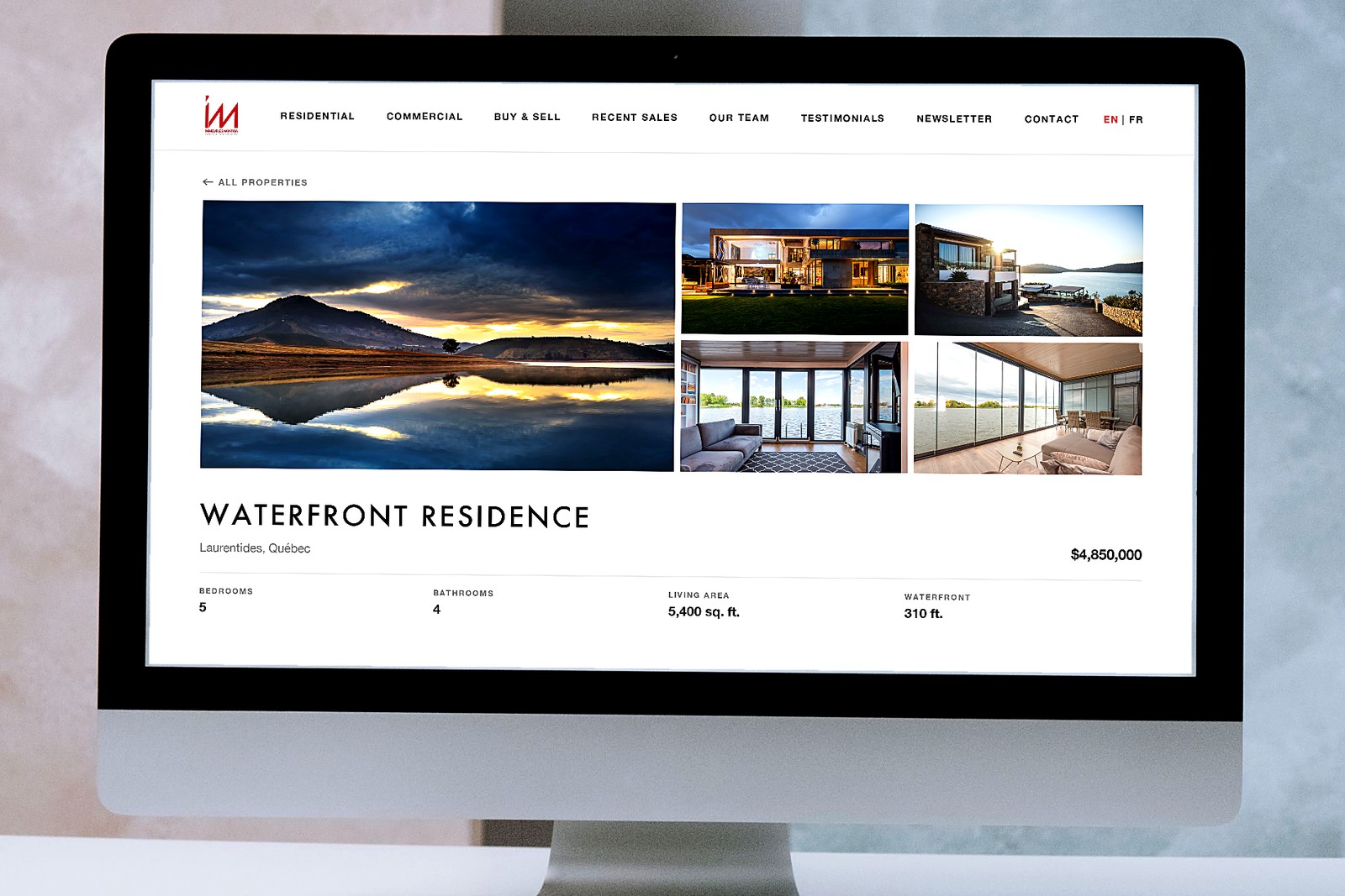 A desktop computer on a white desk showing a Montria listing page for a waterfront residence — a lake at sunset beside photographs of a modern lakeside house.