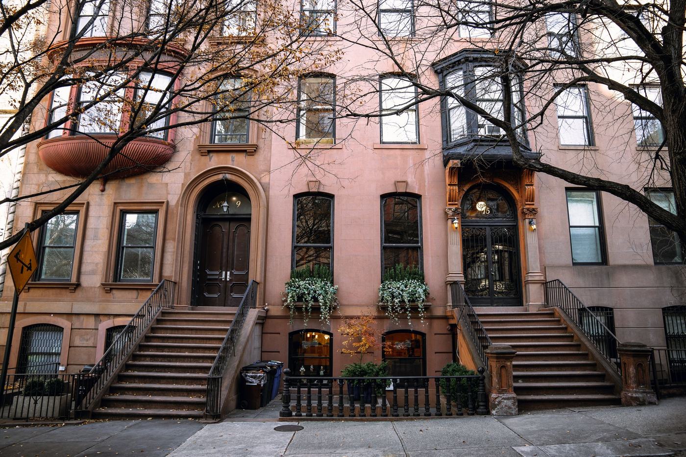 A terrace of brownstone row houses with stoops, arched doorways and window boxes, under bare autumn trees.